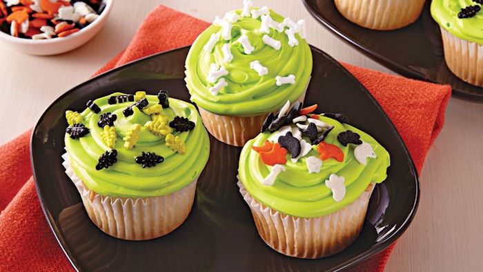 halloween backen, vanille-cupcakes mit grüner creme und kleine figuren aus fondant
