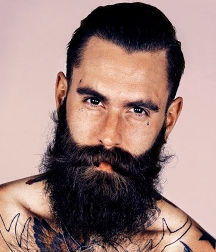 attraktiver Mann mit Brusttattoos, schwarzem langem Bart, Stirntattoo, Wangentattoo