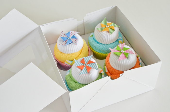 Geschenkideen zur Geburt, vier bunte Cupcakes aus Babysöckchen und Tüchern in weißer Verpackung