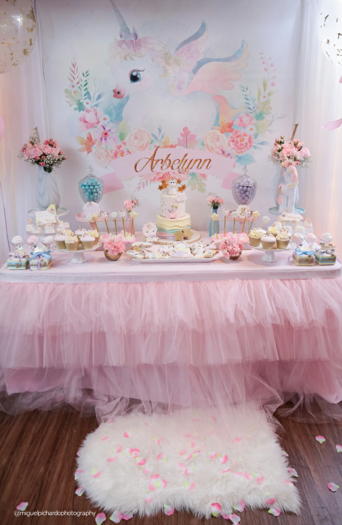 Babyparty für Mädchen, süßes Einhorn an der Wand, Tisch mit rosa Decke, viele Cupcakes und Tarten, zwei große Blumensträusse
