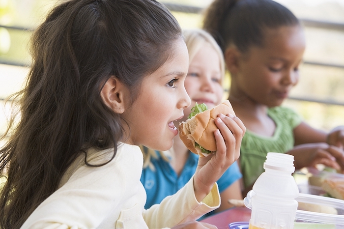 drei kleine Mädchen mit unterschiedlichem Herkunft essen zusammen in der Pause