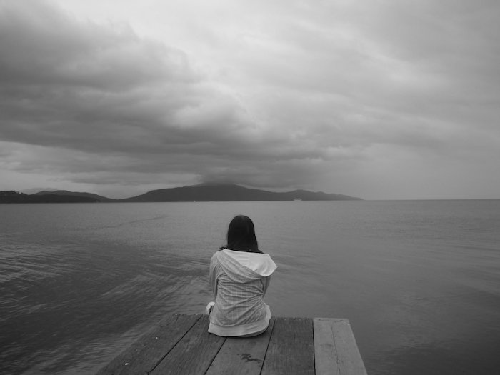 eine junge traurige frau und see und himmel mit grauen wolken - zum thema traurige bilder zum weinen