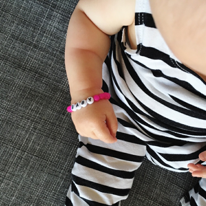 Armband für Baby selber machen, dazu benötigen Sie rosafarbene und weiße Perlen mit Buchstaben