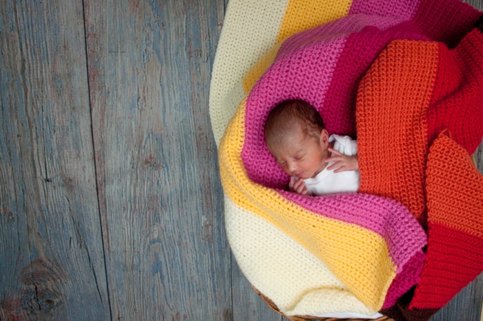 Selbstgestrickte Decke in fröhlichen Farben, süßes schlafendes Baby, Geschenkideen zur Geburt