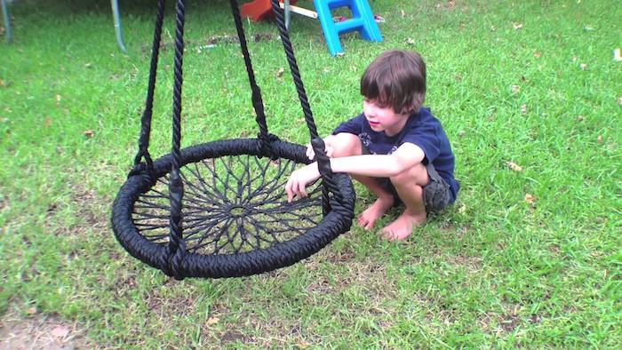 ein Junge auf einer Wiese spielt mit einer schwarzen Schaukel - Kinderschaukel für Garten 