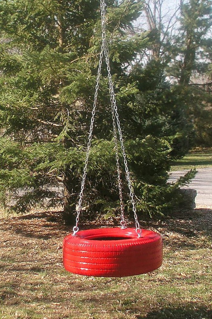 eine Schaukel aus einem roten Reifen mit drei Ketten befestigt in Garten mit vielen Bäumen