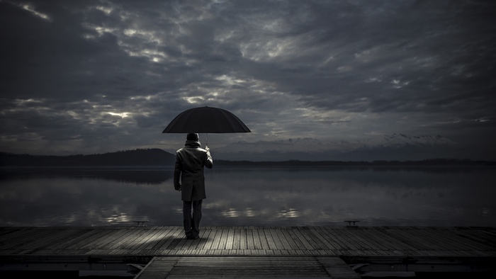 noch ein trauriges bild mit einem einsamen mann mit einem schwarzen regenschirm . meer und himmel mit grauen und schwarzen wolken - traurige bilder zum weinen