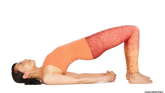 Yoga für Anfänger: asiatische Frau, die die Brückenposition übt, gestreckte Arme und geschlossene Hände, Füße am Boden, Rücken und Po in der Luft