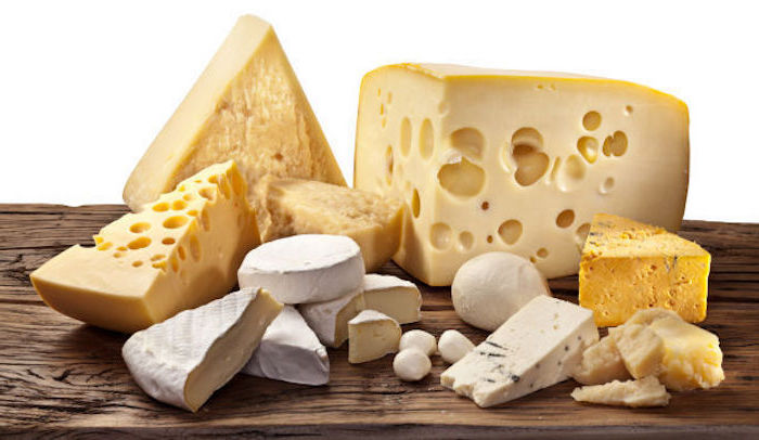 ein Bild mit weißem Hintergrund, das verschiedene Sorten von Hartkäse und Käse mit elastischer Struktur darstellt, drei gepellte Wachteleier neben einem Parmesanlaib, Massivtisch aus Holz mit großen Rissen