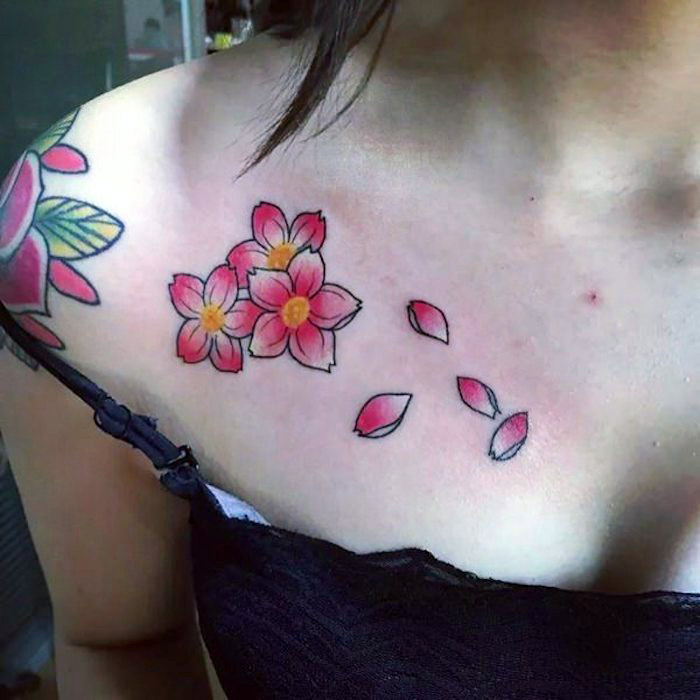 frau mit blumenranke tattoo am schulter, rosa kirschblüten mit wegfliegenden blütenblättern