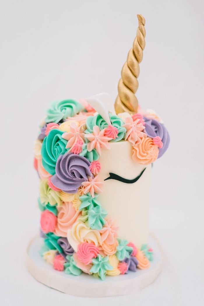 weiße einhorn torte mit einem einhorn mit einer bunten langen mähne aus lila grünen und pinken rosen aus sahne und einem goldenen horn 