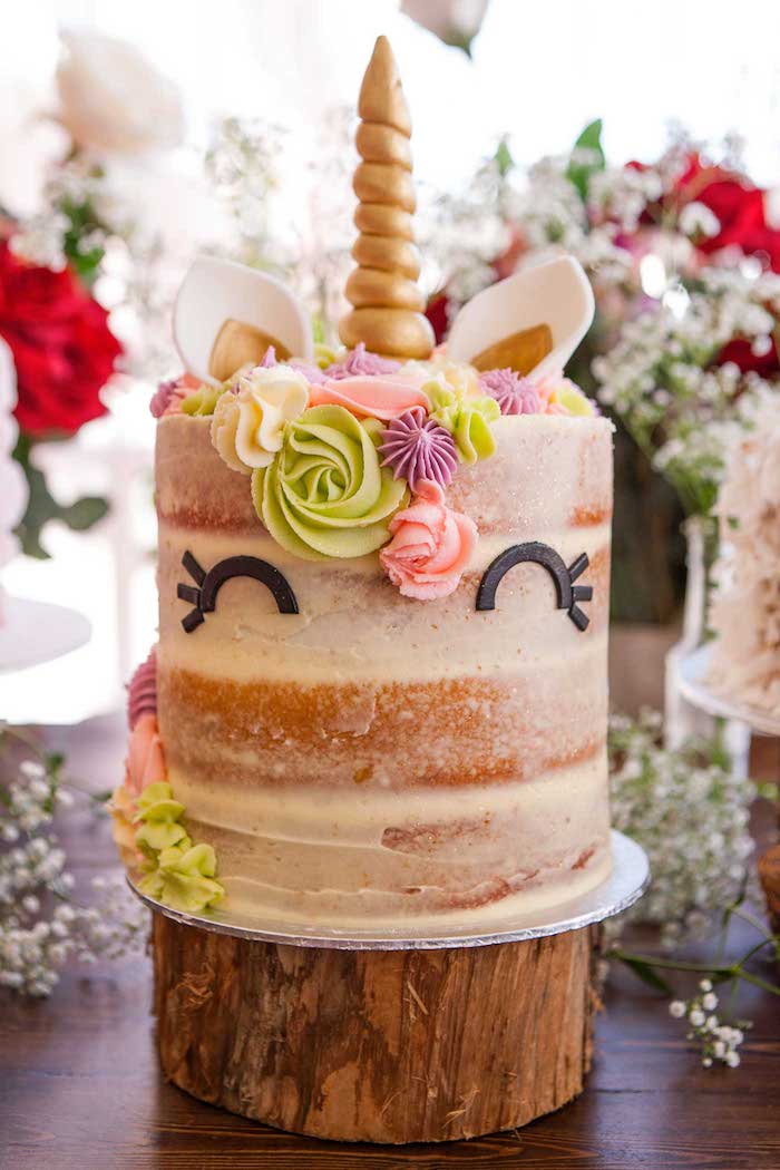 eine große einhorn torte mit schwarzen augen - idee für einhorn kuchen - ein einhorn mit grünen und pinken rosen aus sahne und einem langen goldenen horn