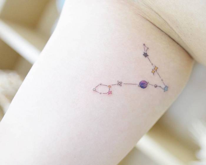 hand mit einem sternbild tattoo mit einem kleinen violetten planet und kleinen blauen und gelben ssternen 