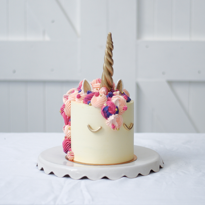 weiße torte mit einem weißen einhorn mit einem langen großen goldenen horn und mit einer langen mähne aus sahne, pinke mähne - idee zum thema einhorn torte und kuchen