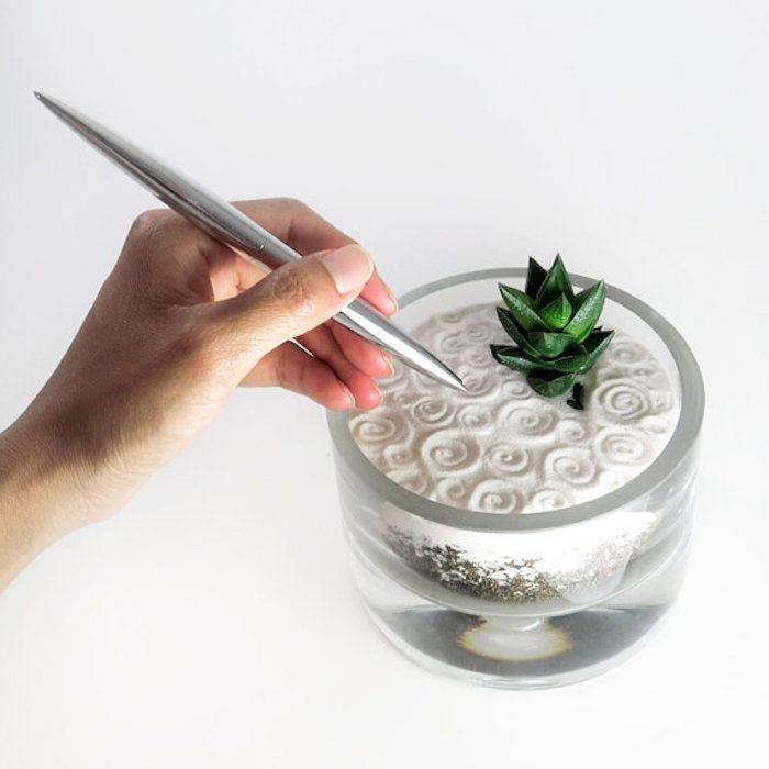 Mini Zengarten in einer Glasschüssel, gefüllt mit weißem Sand, Spiralen mit einem Metallstab in den Sand malen, kleine und sehr grüne Sukkulentpflanze, Minikaktee mit dunkelgrüner Farbe