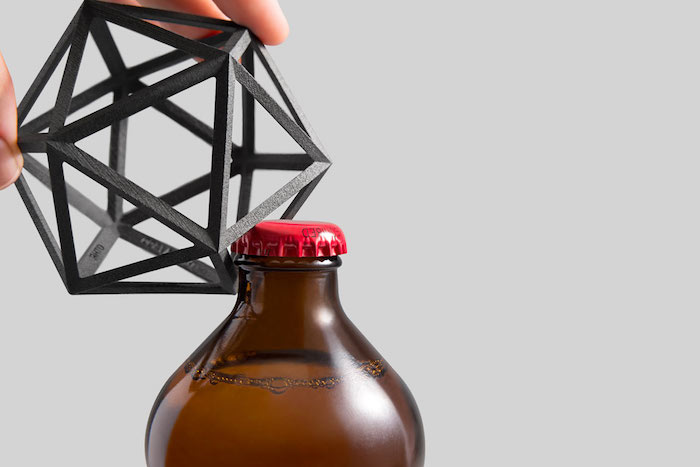Designer Flaschenöffner aus Edelstahl in der Form eines Vieleckes, eine Bierflasche aus braunem Glas mit rotem Deckel aus Metall, ein Mann öffnet eine Bierflasche