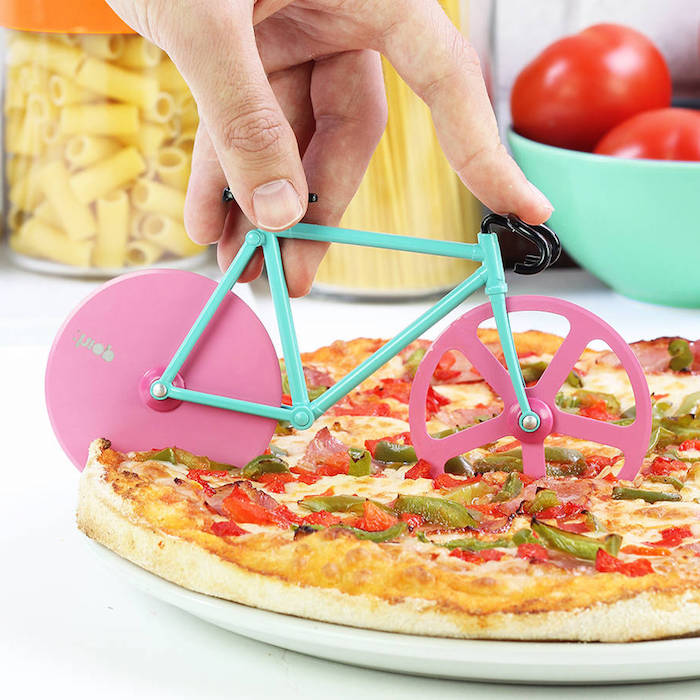 Fahrrad-Pizzamesser mit zwei Schneiden, Fahrrad mit pinken Rädern und türkisblauem Fahrradrahmen, Fahrrad mit schwarzem Fahrradlenker, Plastik-Einmachglas für Pasrta mit orangem Deckel, Spaghetti-Behälter aus Plastik, türkisblaue Schüssel mit zwei roten Tomaten, Pizza-Vegetariana in einem weißen Teller, Pizza mit grünen und roten Paprika 
