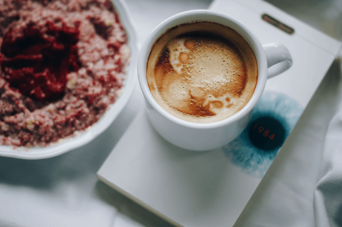 eine kleine Tasse Kaffee mit Milch auf einer weiße Untersilie und ein Kuchen - Guten Morgen Kaffee