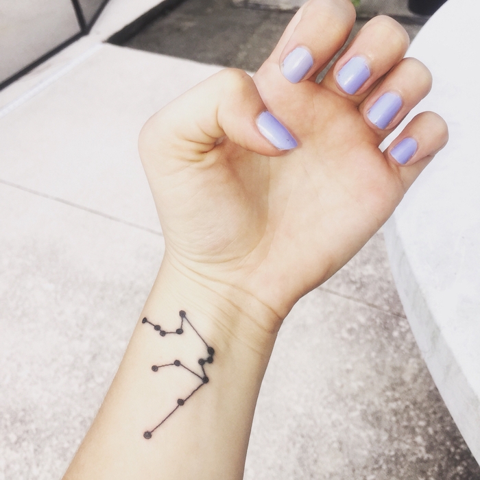 tattoo sterne für frauen - eine hand mit einem violetten nagellack und einem tattoo mit einem schwarzen sternbild auf handgelenk