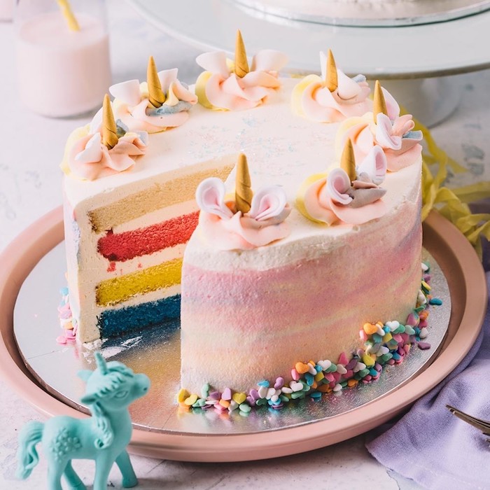 hier ist eine idee für eine pinke torte mit kleinen goldenen gelben hörnern und pinken ohren - regenbogenfarbene einhorn torte und ein kleines blaues einhorn - idee für einhorn kuchen deko