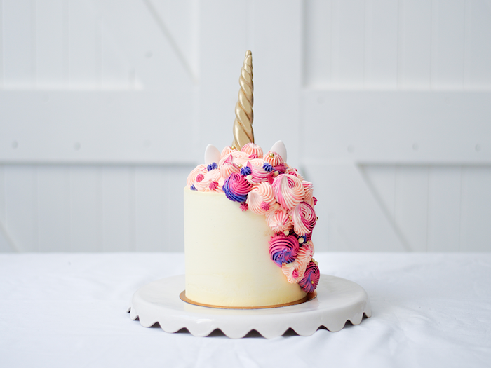 ein weißes einhorn mit einem langen goldenen horn - eine weiße torte mit einer langen mähne aus einer pinken sahne und mit lila und pinken rosen