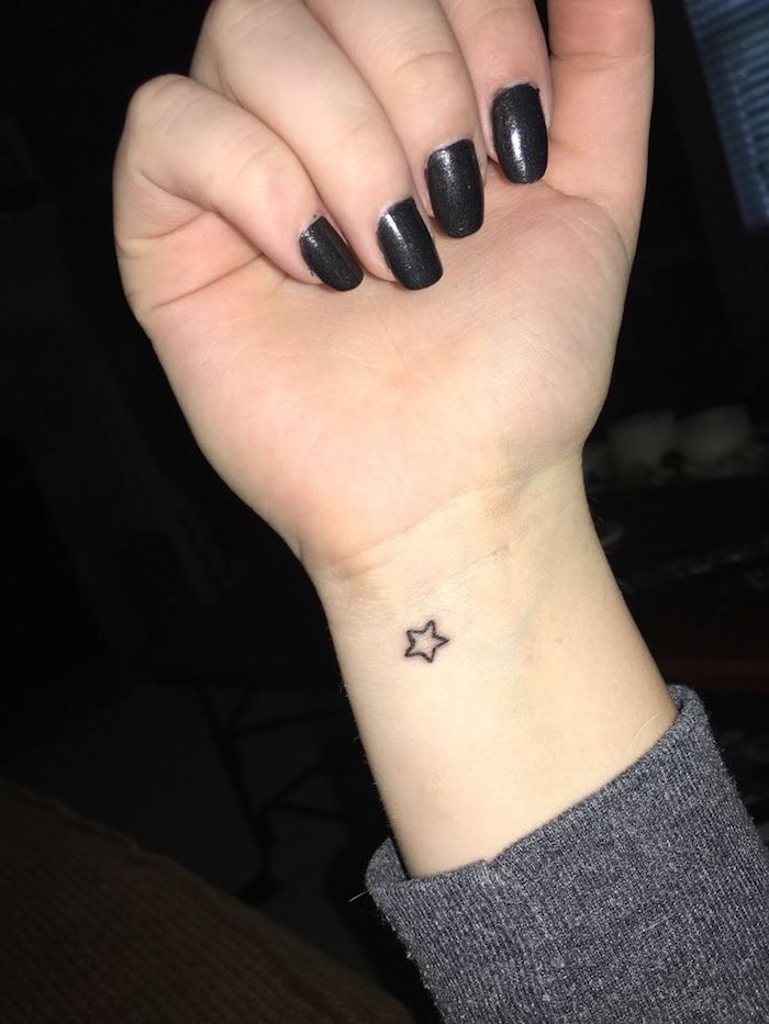 eine hand mit einem kleinen schwarzen tattoo mit einem kleinen stern - hand mit nägeln mit einem schwarzen nagellack 
