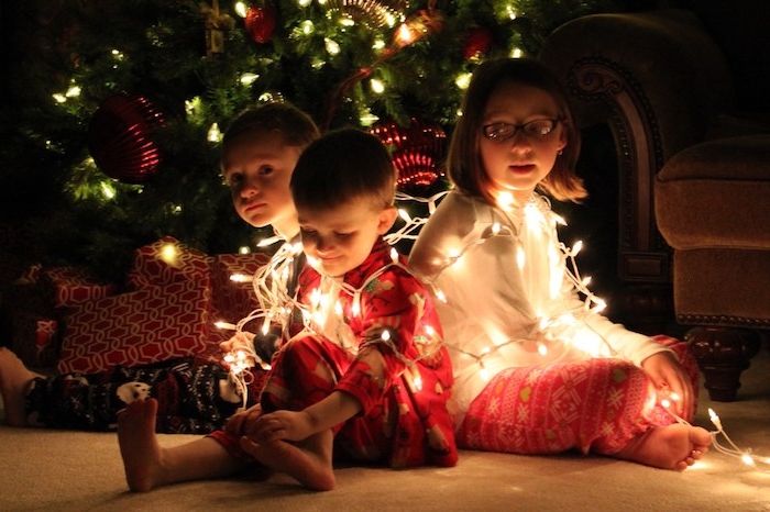 lustige Weihnachten drei niedliche Kinder spielen mit einer Lichterkette vor dem Weihnachtsbaum