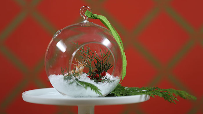 Glaskugel für Weihnachtsbaum mit rundem Loch, Miniatur von Elchen, kleine rote Beeren, Zweig vom Weihnachtsbaum, rote Tapeten mit grünem Muster 