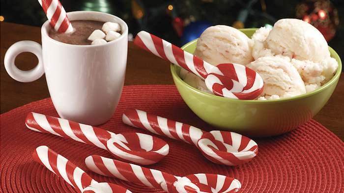 Kakaogetränk mit Marshmallows in weißer Porzellantasse mit rundem Henkel, rot-weiße Karamellutscher in der Form von Teelöffeln, Vanille-Eis in grüner Schüssel