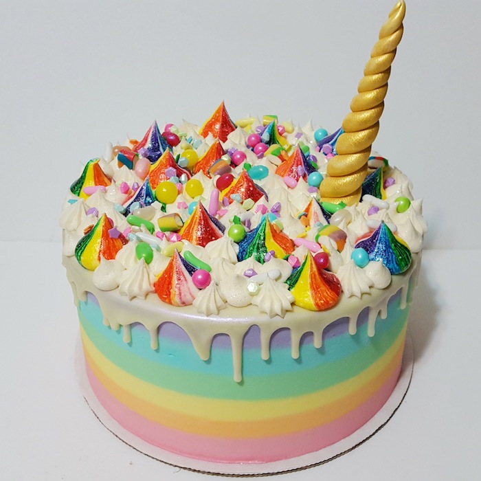 noch eine regenbogenfarbene torte mit einer weißen sahne und einem großen langen goldenen horn - idee für einhorn kuchen deko