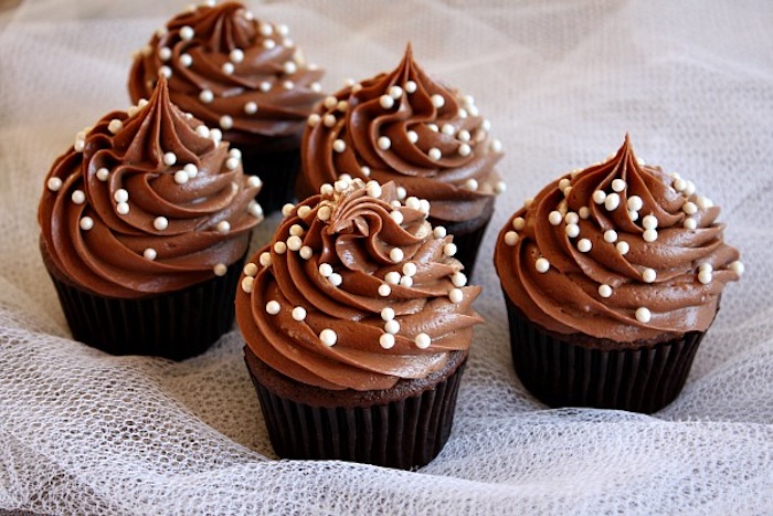 Schoko-Cupcakes mit Schokoguss, bestreut mit Schokoladenperlen aus weißer Schokolade, braune Cupcake-Förmchen
