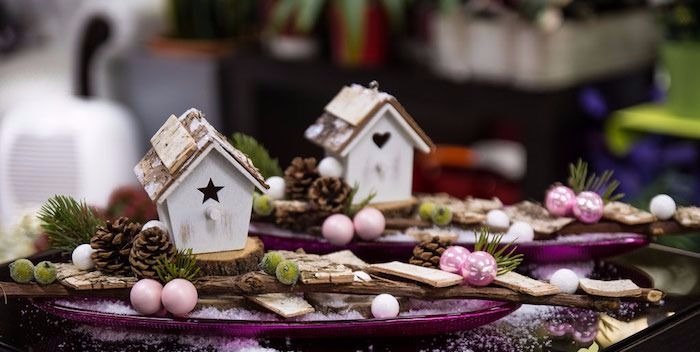 zwei hölzerne Häuser mit Löchern in der Form eines Sternes und eines Herzens, dekorative Glasteller in Violettfarbe, Deko mit Zapfen und Tannenbaumzweigen, Glastisch, dekoriert mit künstlichem Schnee