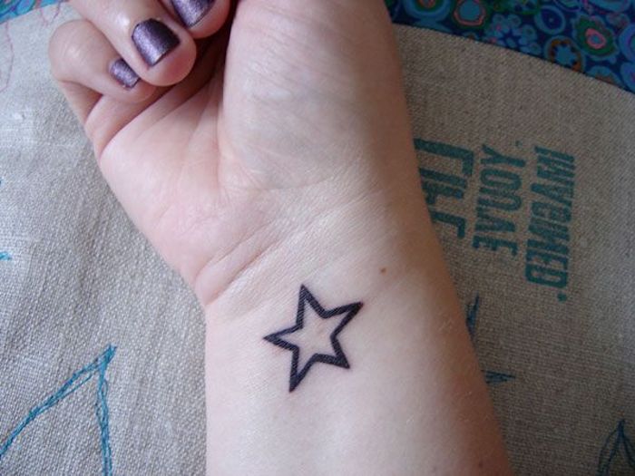 hand mit einem violetten nagellack und einem kleinen schwarzen stern tattoo
