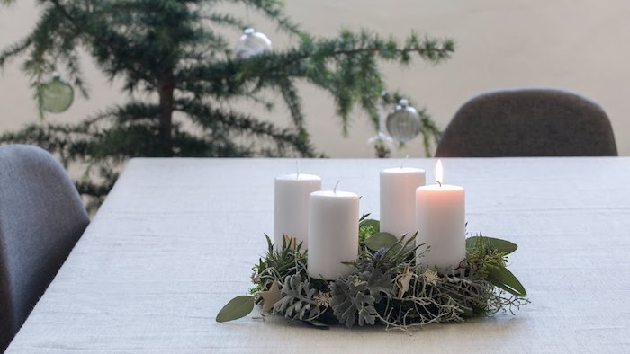 ein tisch mit einem kleinen adventskranz mit vier weißen kerzen und mot pflanzen mit grünen blättern