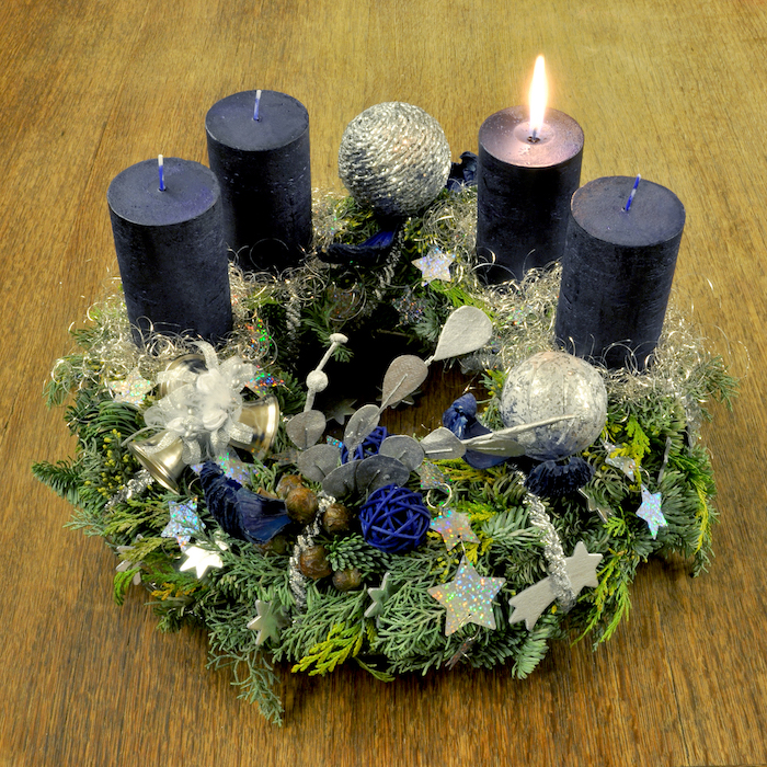 ein adventskranz mit vier kleinen blauen kerzen, mit grünen pflanzen mit grünen blättern und kleinen sternen und bällen 