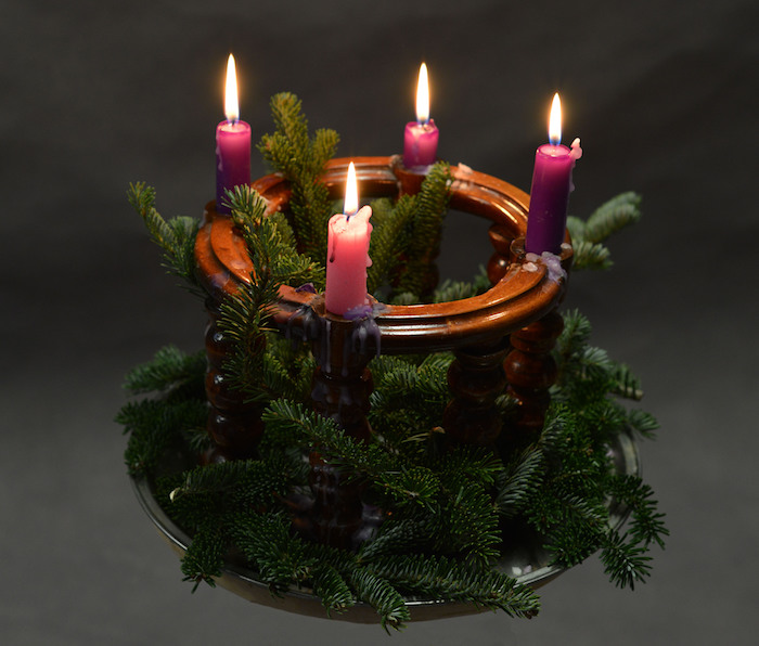 einen kleinen adventskranz mit ästen und drei lila kerzen und einer pinken kleinen kerze