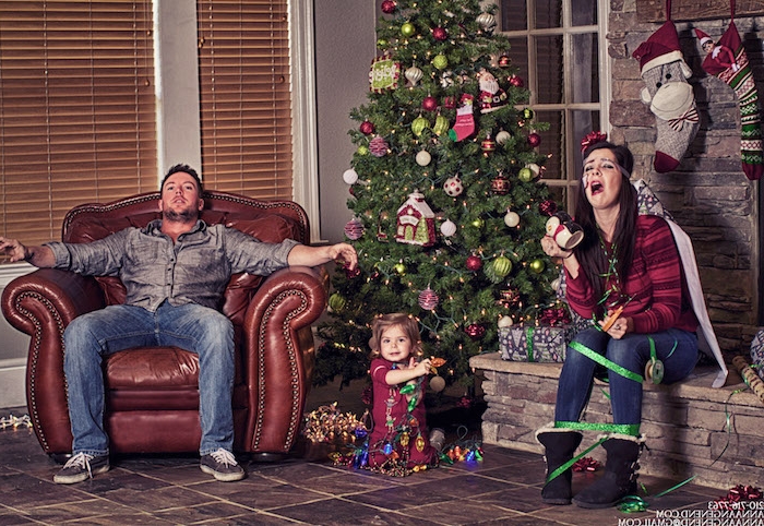 eine lustige Familie um dem Tannenbaum, der Vater sieht erschöpft aus, die Mutter ist im Geschenkband umhüllt, nur die kleine Prinzessin ist glücklich - Weihnachtsfotos