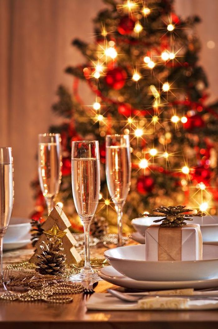 deko weihnachten tischdekor ideen zum gestalten drei gläser voll mit weißwein perlen als deko auf dem tisch weihnachtsbaum im hintergrund