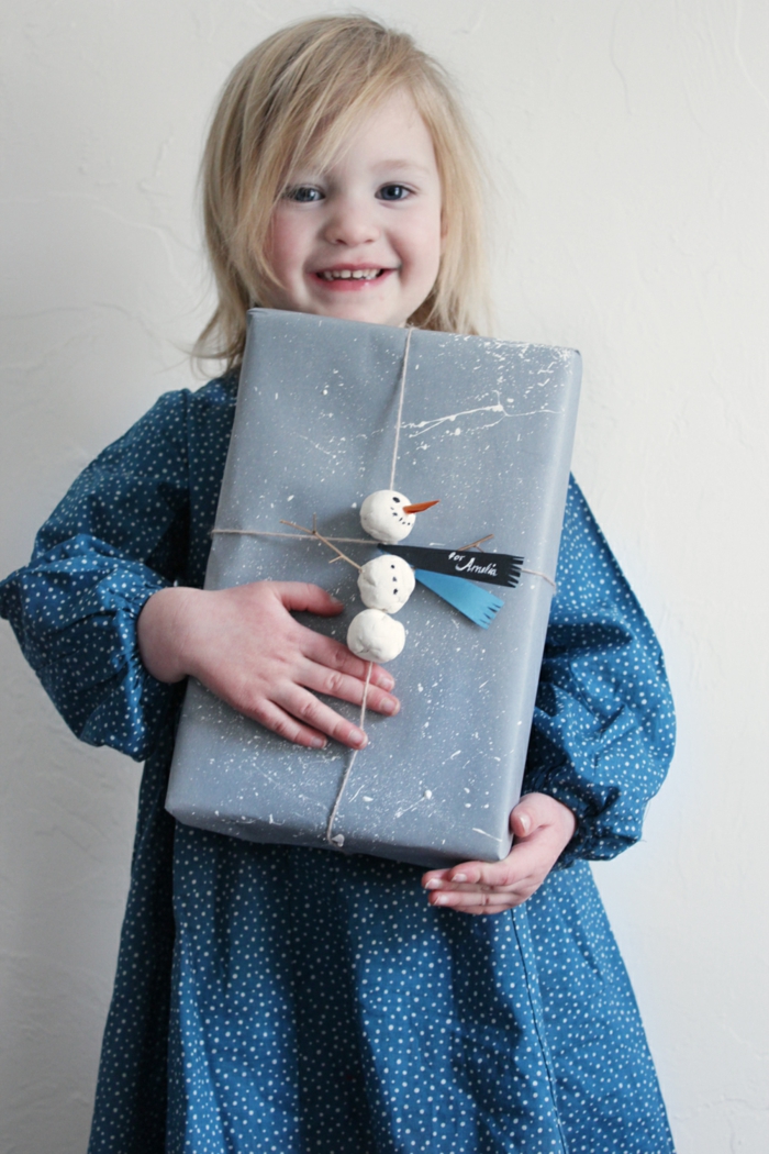 Schneemann aus Plastilin basteln und Weihnachtsgeschenk verpacken, blondes Kind mit großen schwarzen Augen