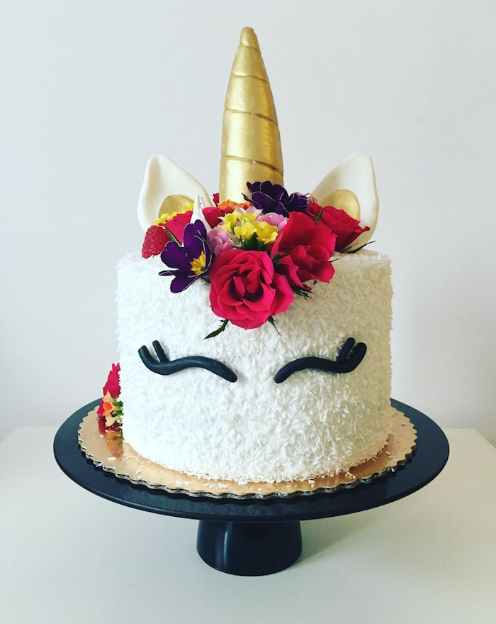 hier ist eine weiße torte mit einem einhorn mit schwarzen augen und mit roten rosen und lila blumen und einem großen goldenen horn