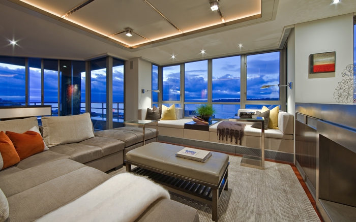 großes Wohnzimmer, gestaltet in Grau, offene Feuerstelle, indirekte LED-eleuchtung, riesige Fenster
