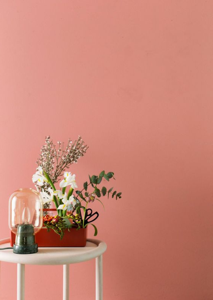 Apricot Wandfarbe, weißer Tisch, roter Blumentopf mit verschiedenen Blumen, Retro Nachttisch Lampe
