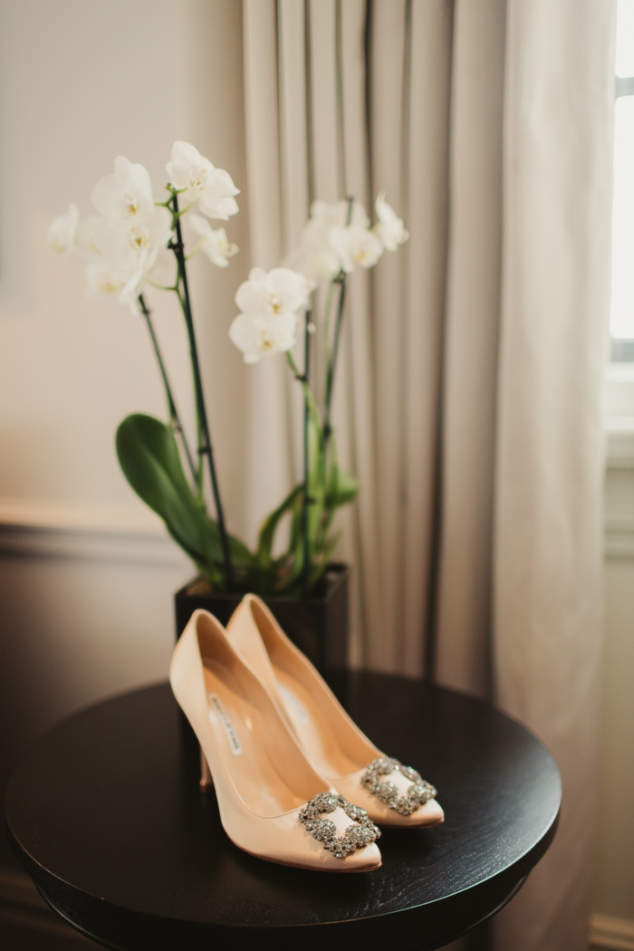 High Heels in Apricot mit Kristallen auf schwarzem Tisch, weiße Orchidee, elegante Hochzeitsschuhe