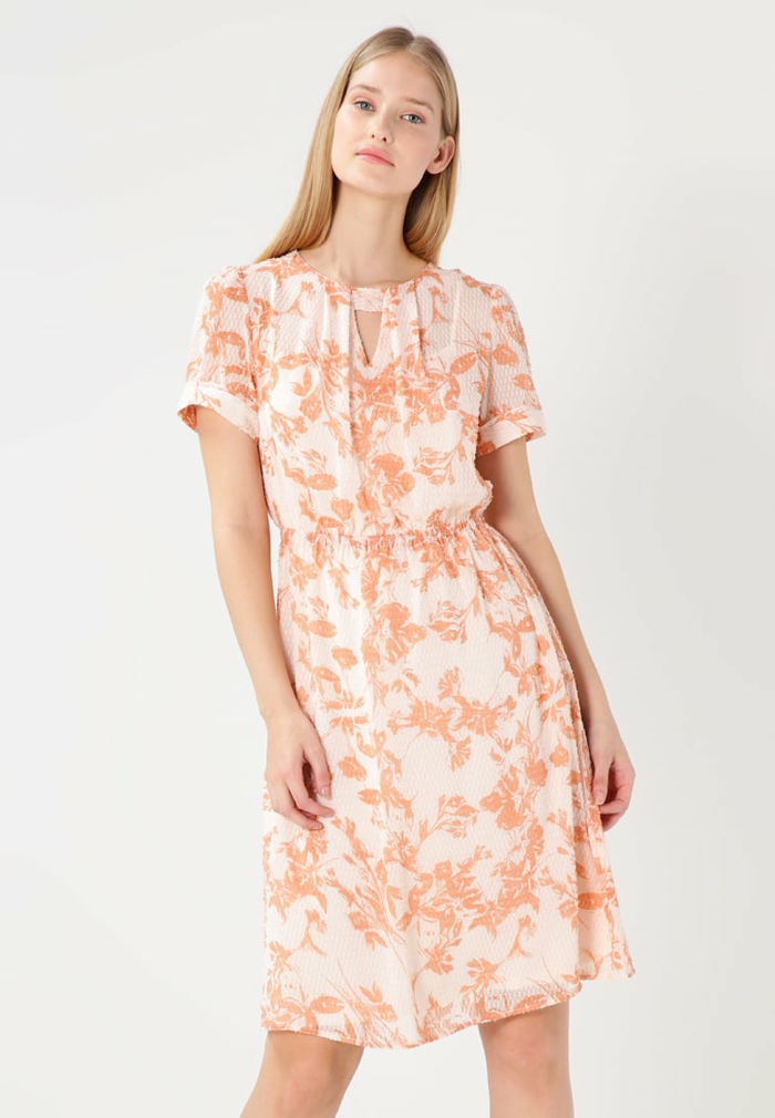 Sommerkleid in Weiß und Apricot mit Blumenmuster, kurze Ärmel, Frau mit blonden langen Haaren, rosafarbene Lippen