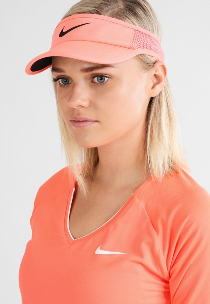 Nike T-Shirt und Baseballcap in Apricot, blonde glatte Haare, blaue Augen, matter Lippenstift und schwarze Mascara