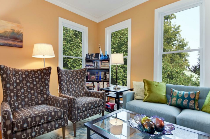 Wohnzimmer Einrichtung, Wandfarbe Apricot, blaues Sofa mit bunten Dekokissen, braune Sessel, Glasschale voll mit Kunstobst
