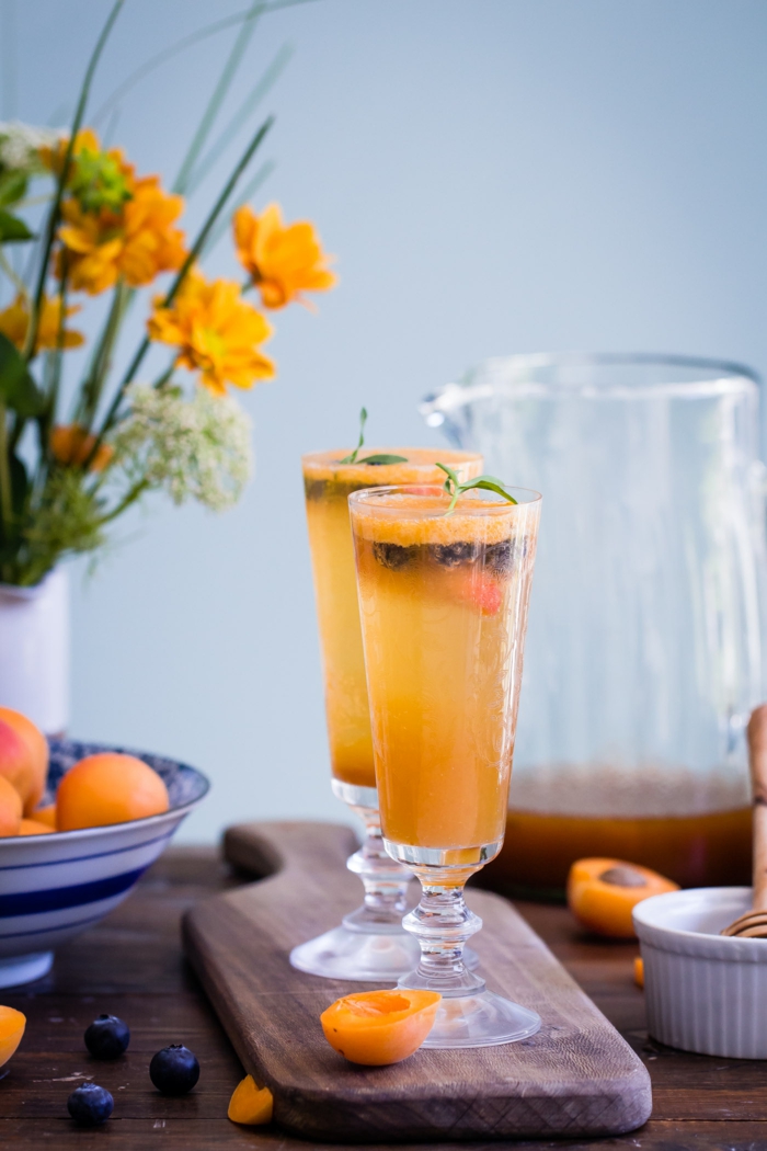 Cocktails mit Aprikosen, oranger Blumenstrauss in Porzellanvase, Blaubeeren und Aprikosenscheiben