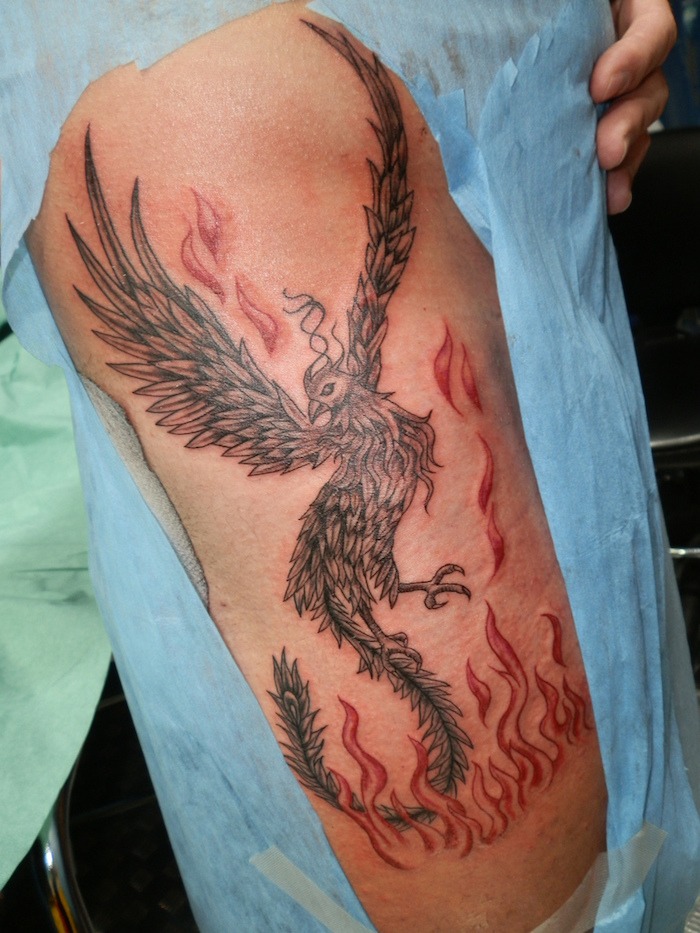 mann mit einem großen schwarzen tattoo mit einem schwarzen fliegenden phönix mit schwarzen federn und feuer - phönix aus der asche tattoo, phönix Tattoo Oberarm