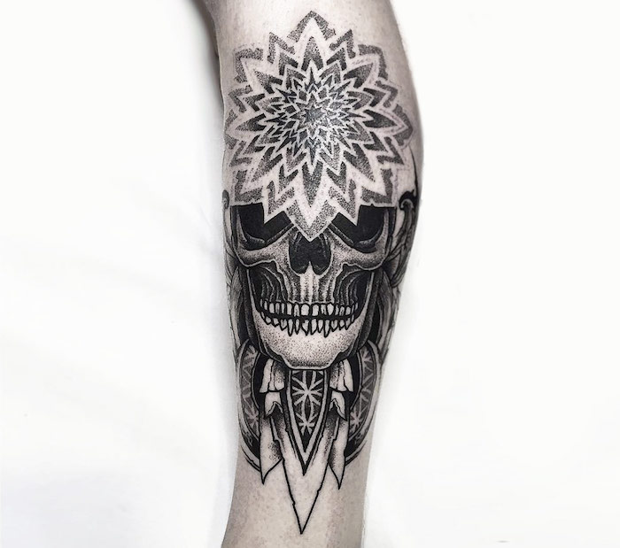eine hand mit einem traumfänger tattoo mit einem weißen totenkopf mit schwarzen augen und weißen zähnen udn federn