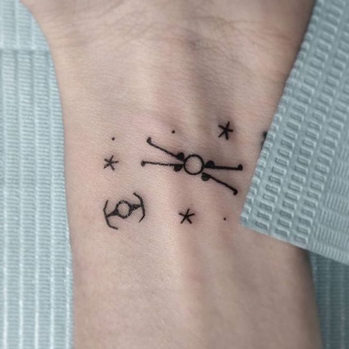 idee für einen star wars tattoo am handgelenk - ein schwarzer kleiner tattoo mit kleinen schwarzen sternen und planeten und kleinen fliegenden star wars raumschiffen